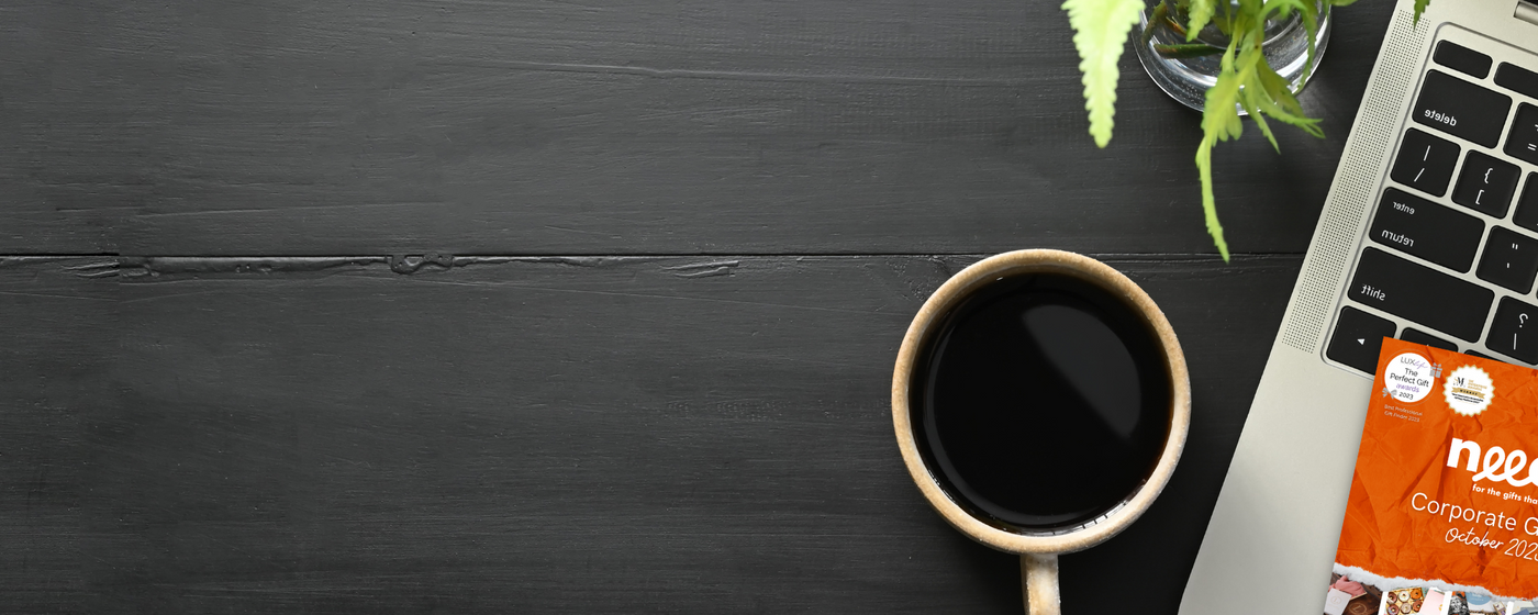 A dark wooden desktop with a black coffee, laptop and the edge of a corporate gift guide